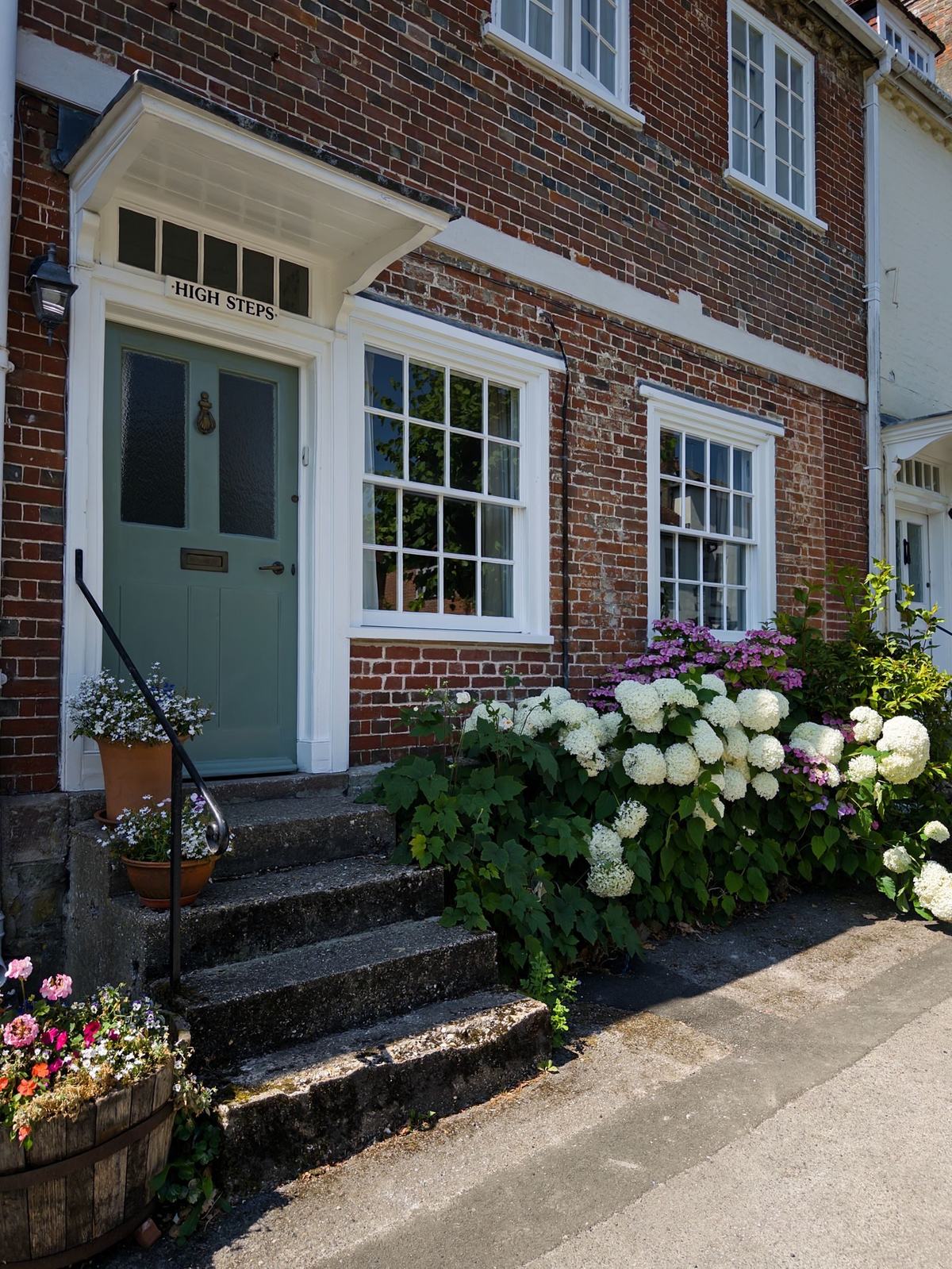 A red-brick house with bright white windows and flowering shrubs